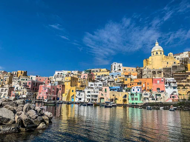 dozens of pastel colored houses that make up a fishing village on the island of Procia seen from the boat