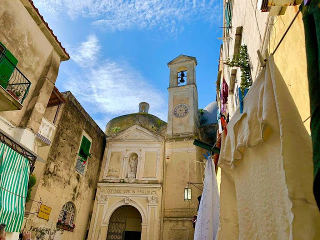 a small abbey with its bell tower inside a narrow alley where from a terrace clothes are laid to dry