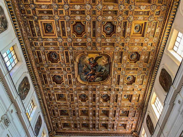 a golden wooden ceiling with a honeycomb shape made of larger and smaller rectangles with a fresco in the center